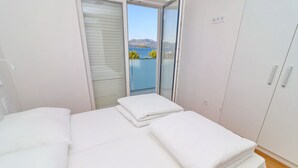 Un dormitorio con cama, cortinas blancas, vista al mar y un armario.