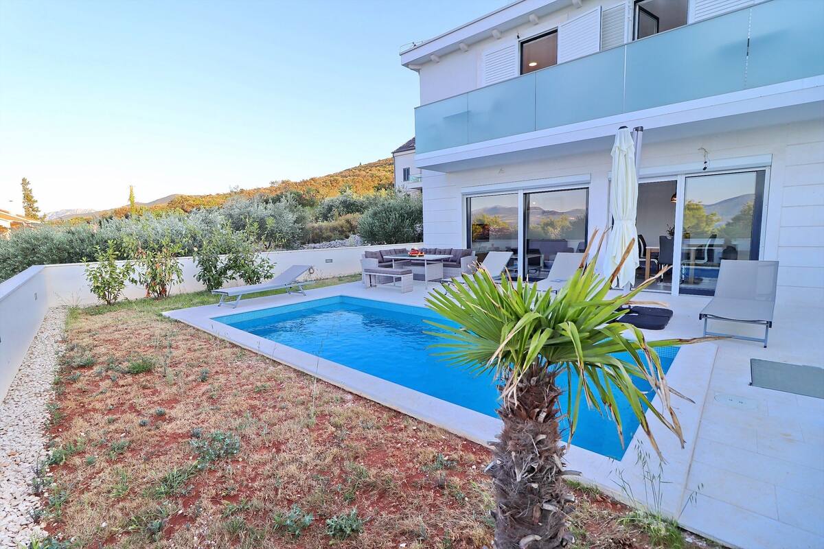 A modern house with a swimming pool, outdoor seating, and a view of the hills.