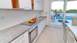 Una cocina moderna con armarios blancos, encimera de acero inoxidable y vista a una piscina a través de una puerta de vidrio.