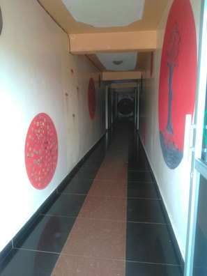 A corridor with tiled floors, red circular wall decorations, and a large red and black mural on the right wall.
