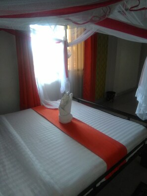 A single bed with a white mattress, a red bedspread, and a white towel placed on the bed. - Lakers Tavern Lounge (Kisumu)