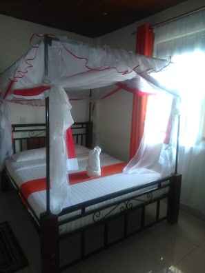 A four-poster bed with a canopy, a white towel, and a red accent.