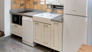 Eine Küche mit weißen Schränken, einer Granitarbeitsplatte, einer Edelstahlspüle, einem Geschirrspüler und einem Kühlschrank.