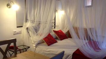 Une pièce avec un lit recouvert d’un voile blanc, deux oreillers rouges, une table en bois et une chaise.