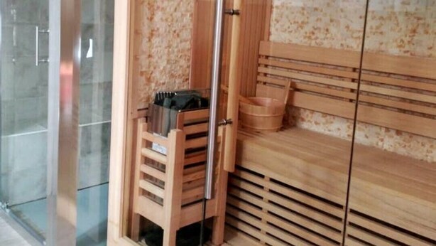 Ein Saunaraum mit einer Holzb bank, einer Glastür und einem gefliesten Boden.