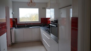A modern kitchen with white cabinets, a red backsplash, a window, and a hanging light fixture.