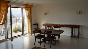 A dining area with a table and chairs, a chandelier, and a view through a large window with curtains.