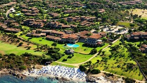 An aerial view of a coastal resort with villas, a swimming pool, and a beach area with umbrellas. - Lovely apartment in villa for 6 guests with A/C, pool, TV and terrace (San Teodoro)