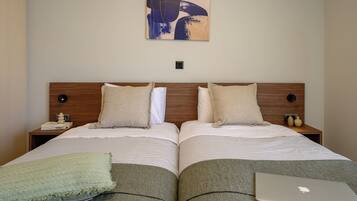 A double bed with two pillows, a bedside table with a lamp, a wall art piece, and a laptop on the bed.