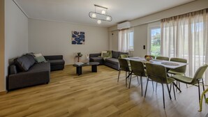 A modern living room with a sectional sofa, a dining table with chairs, a coffee table, and a ceiling light fixture. - Elise Apartment Airport  by Airstay (Spata-Artemida)