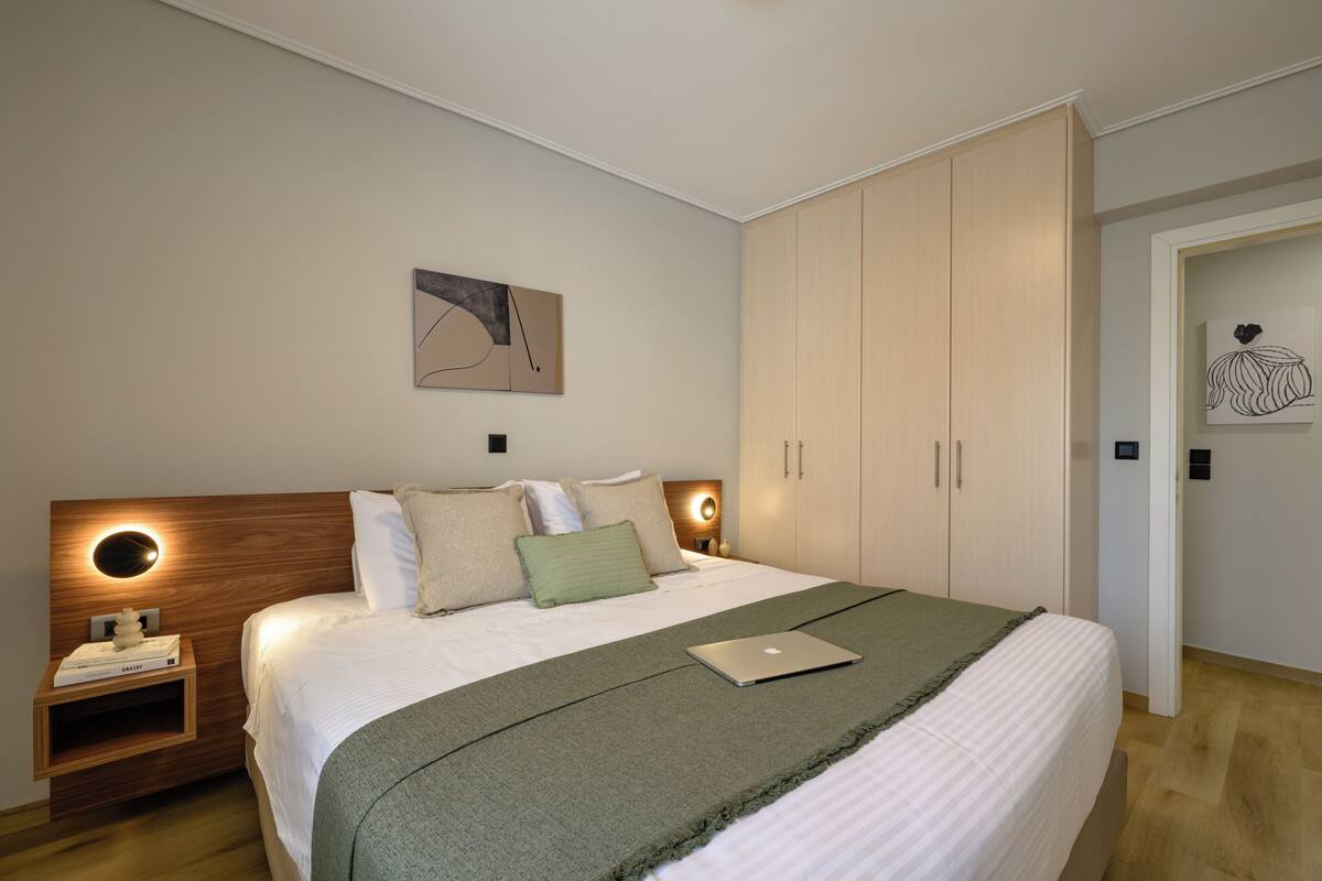 A bedroom with a bed, bedside table, lamp, artwork, and wardrobe.