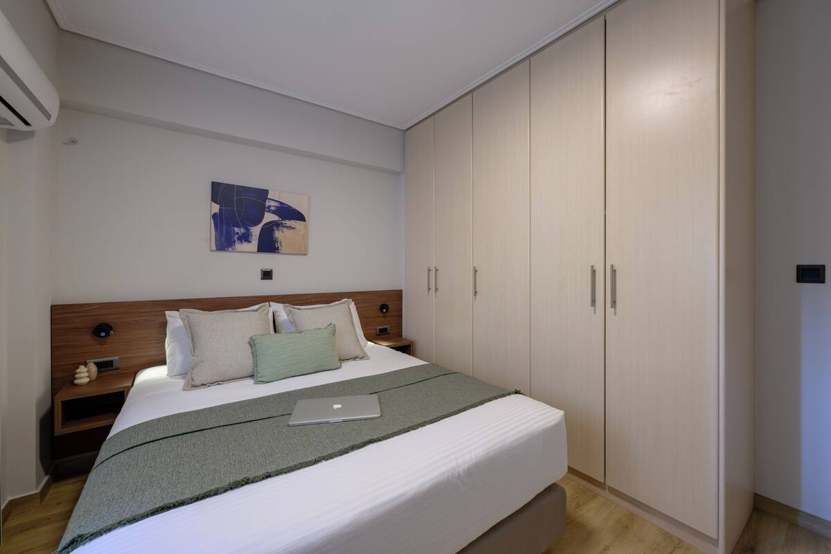 A bedroom with a bed, a laptop, a nightstand, a wall art piece, and a wardrobe.