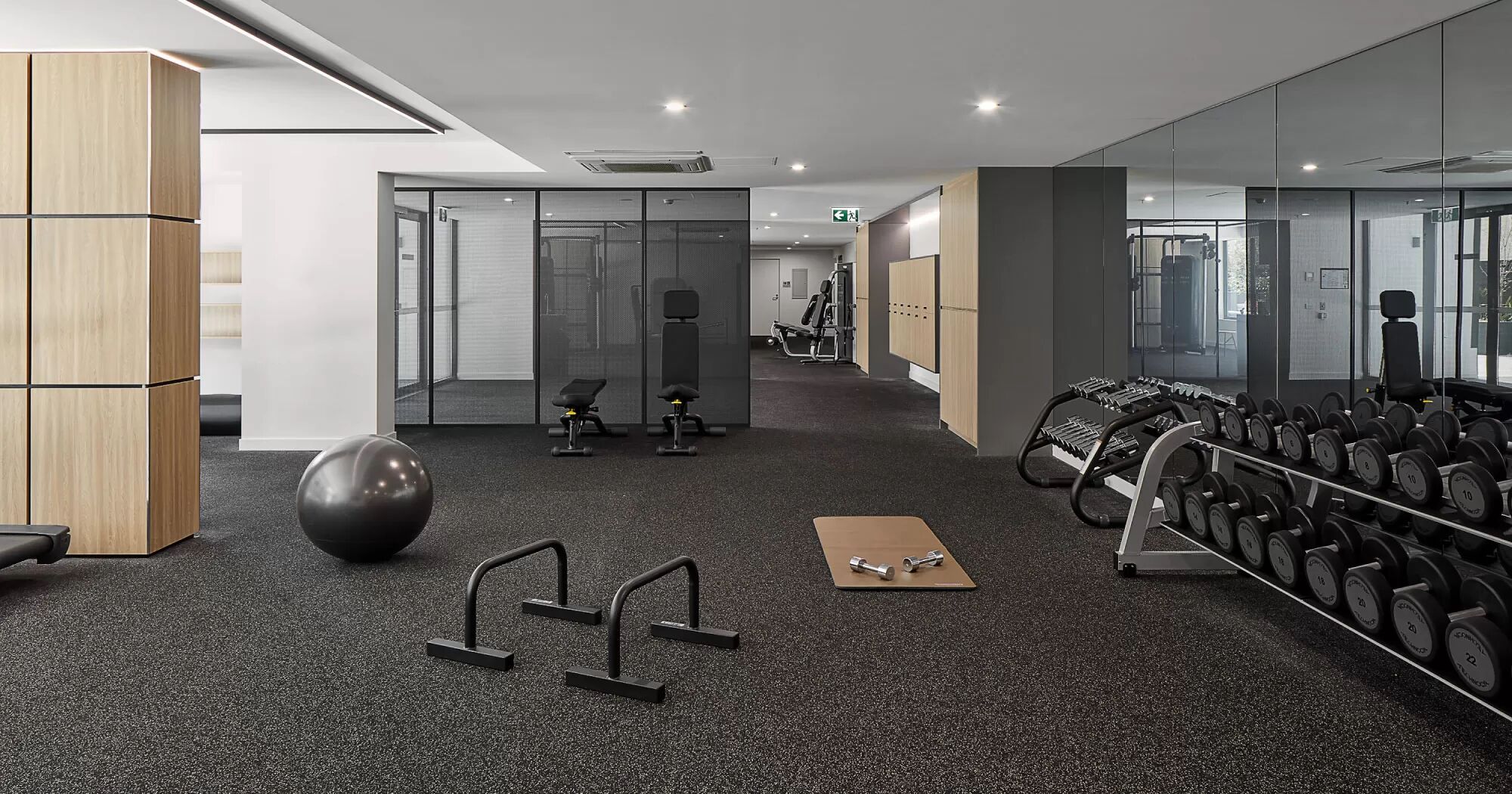Ein modernes Fitnessstudio mit Trainingsgeräten, einem großen Spiegel und einem Teppichboden.