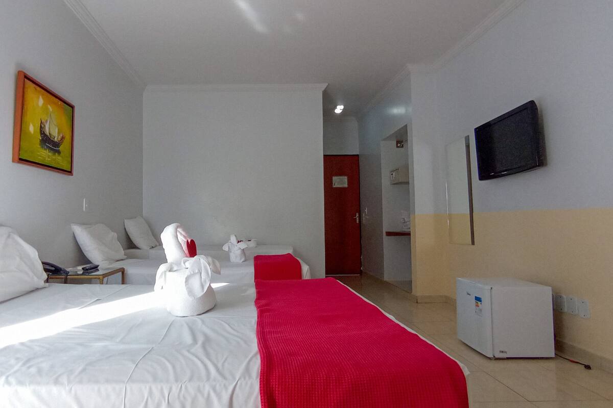 A hotel room with two beds, a TV, a small fridge, and a painting on the wall.