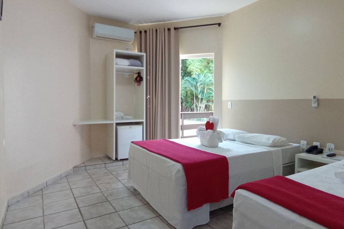A hotel room with two beds, a small desk, a wardrobe, and a window with curtains.