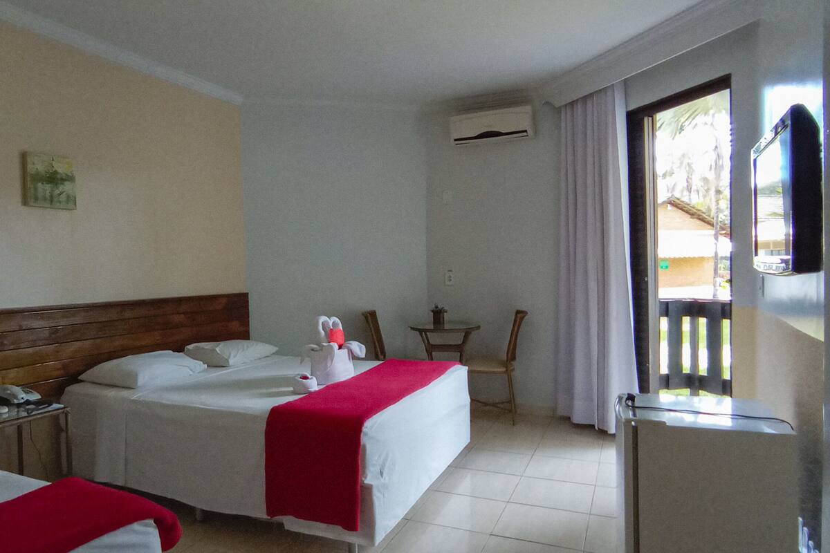 A hotel room with two beds, a small table, a chair, and a window with curtains.