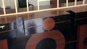Un comptoir d’accueil avec un comptoir en bois et une cloison en verre. Derrière le comptoir, on trouve une vitrine murale où sont exposés divers objets.