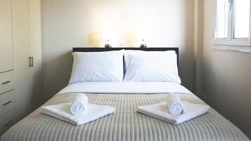 Una cama bien hecha con sábanas blancas y dos toallas enrolladas sobre la cama.