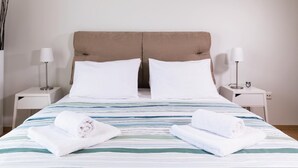A neatly made bed with striped bedding, two pillows, and two rolled towels on the bed. - Anivia Apartment Airport by Airstay (Spata-Artemida)
