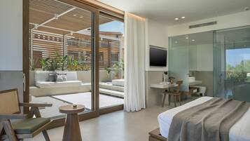 A modern hotel room with a large sliding glass door leading to a balcony, a bed with a grey blanket, a desk with a chair, and a TV mounted on the wall.