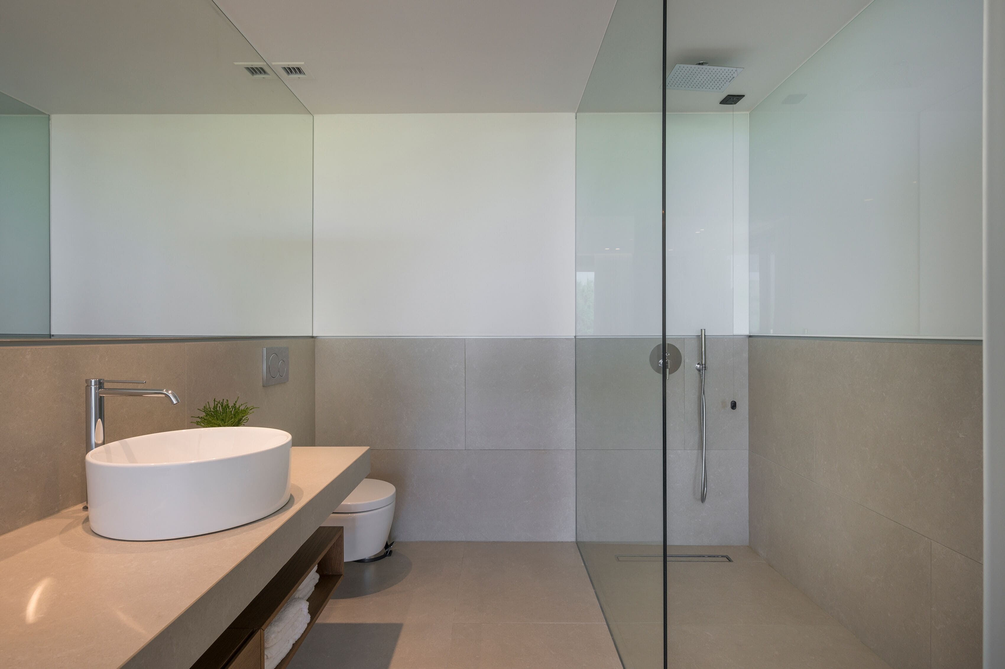 A modern bathroom with a round sink, a toilet, and a glass shower enclosure.