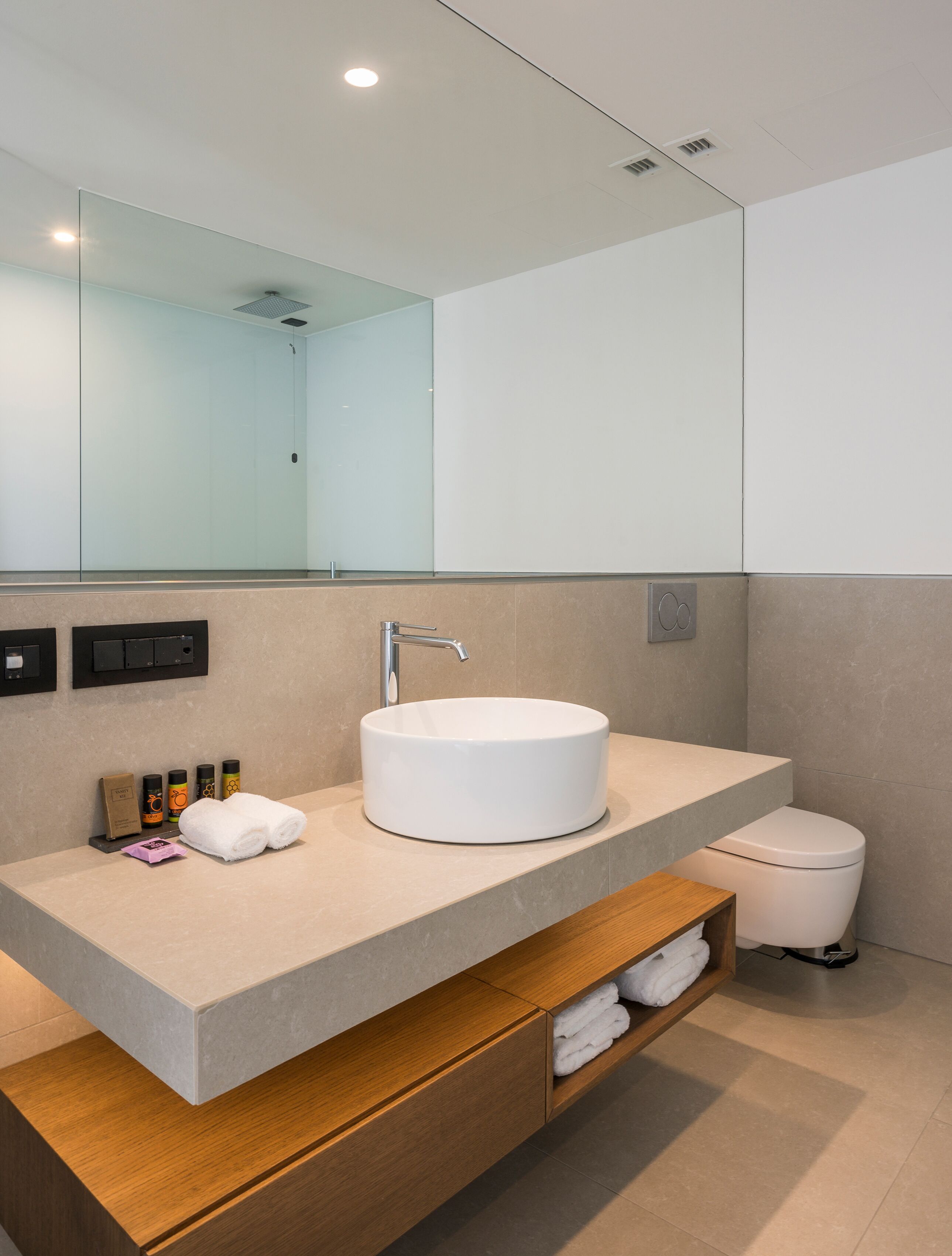 A modern bathroom with a round white sink, a mirror, a shower, and a toilet.