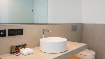 A modern bathroom with a round white sink, a mirror, a shower, and a toilet.