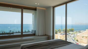 Une chambre dotée d’une grande fenêtre donnant sur la côte, avec un lit et un coin salon offrant une vue sur la mer.