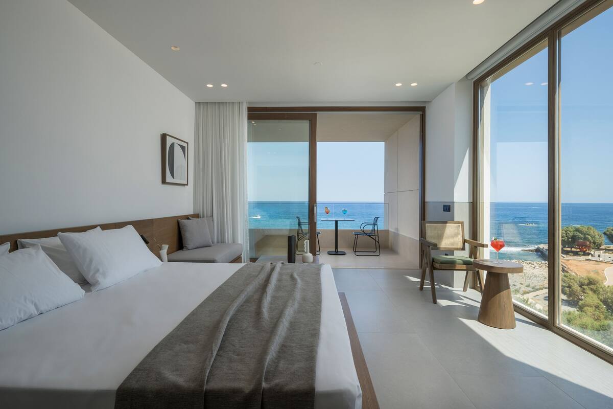 Ein modernes Hotelzimmer mit einem großen Bett, einem Balkon mit Meerblick und einem kleinen Tisch mit Stühlen.