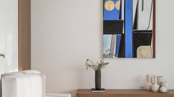 Un salon moderne au design minimaliste, comprenant un canapé, une table basse, un vase avec une plante et un tableau abstrait accroché au mur.