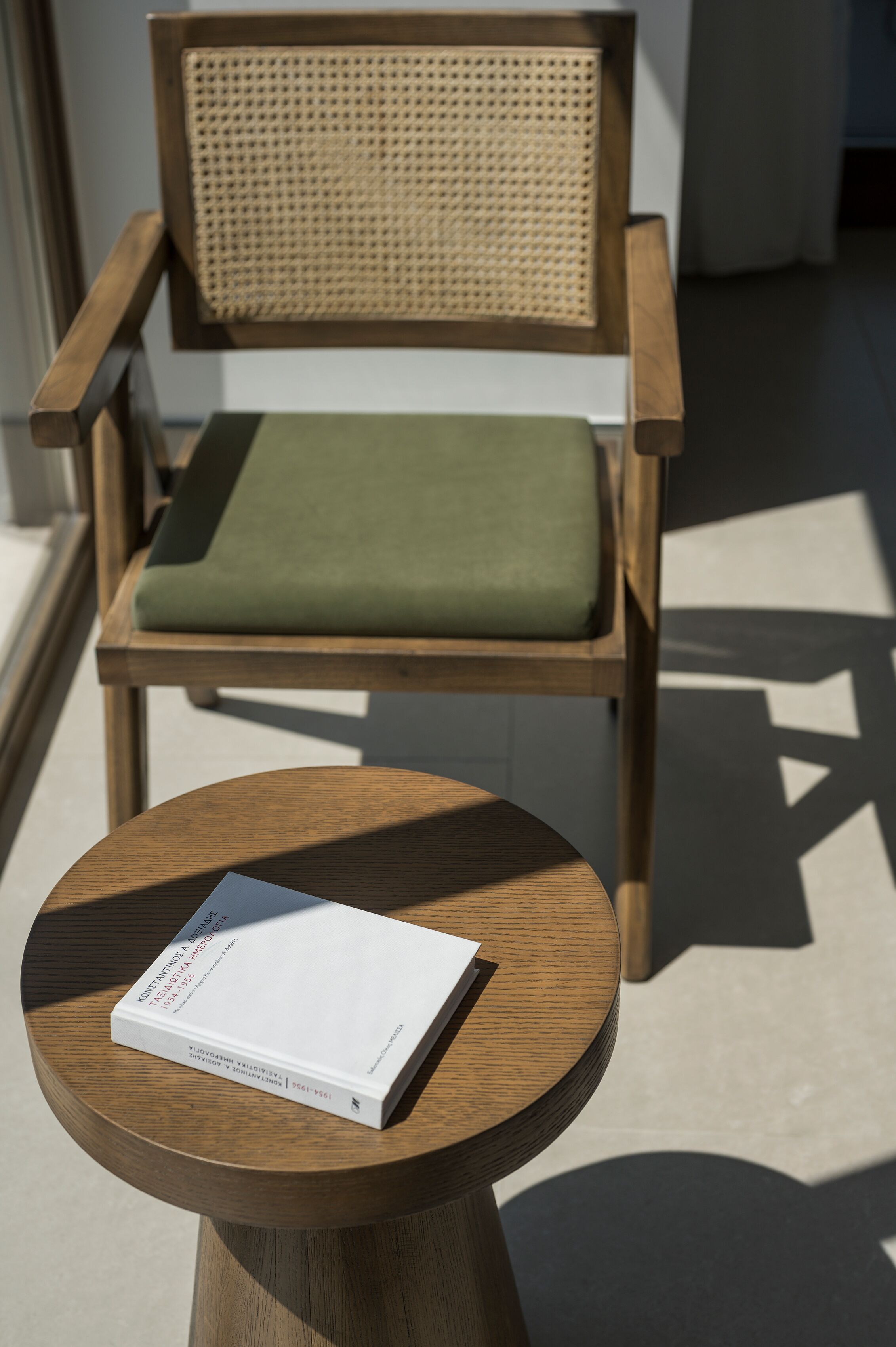 Una silla de madera con un cojín verde y una mesa redonda de madera con un libro encima.