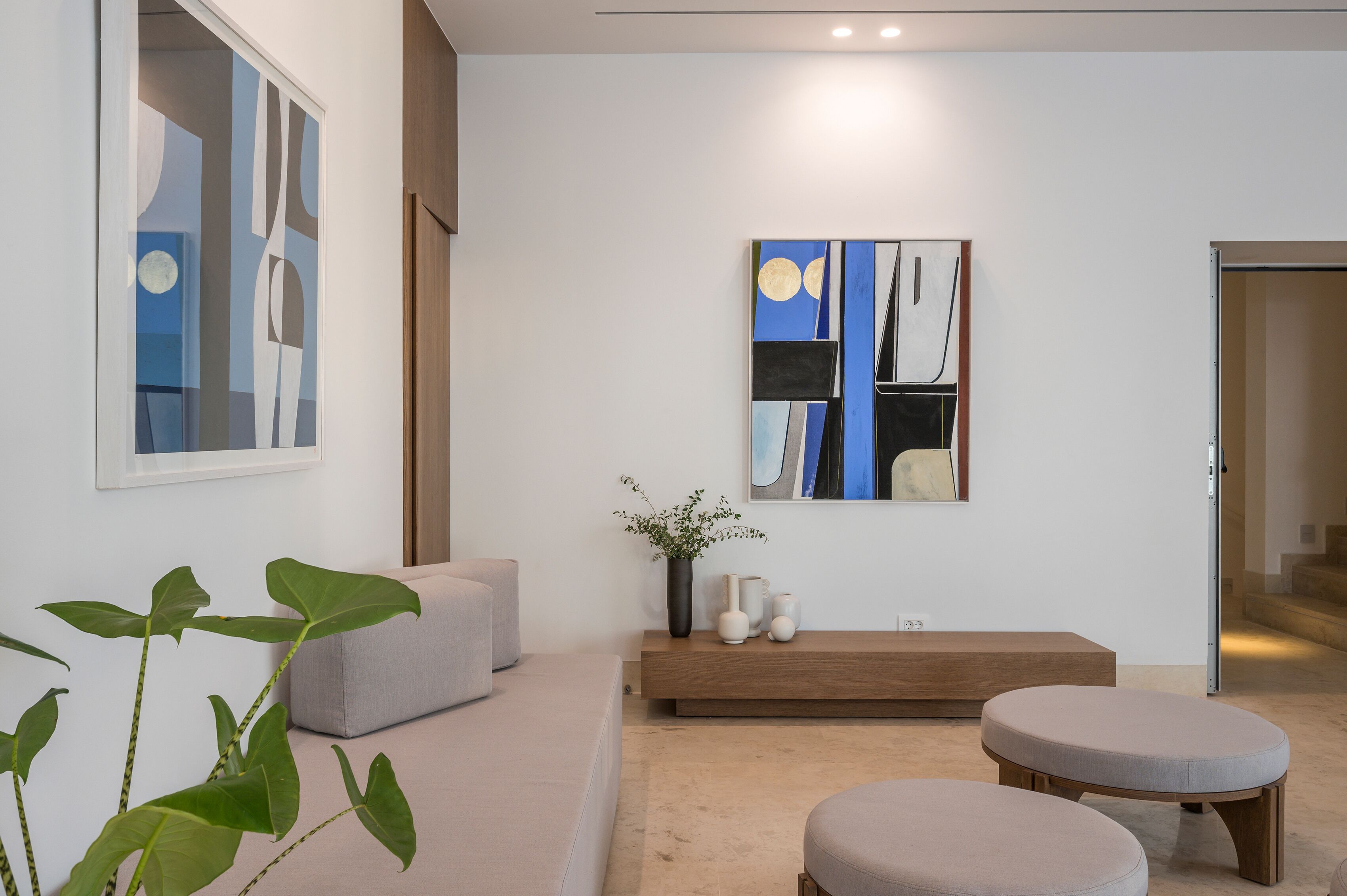 Una sala de estar moderna con un cuadro abstracto grande, un sofá, un banco y una planta en maceta.