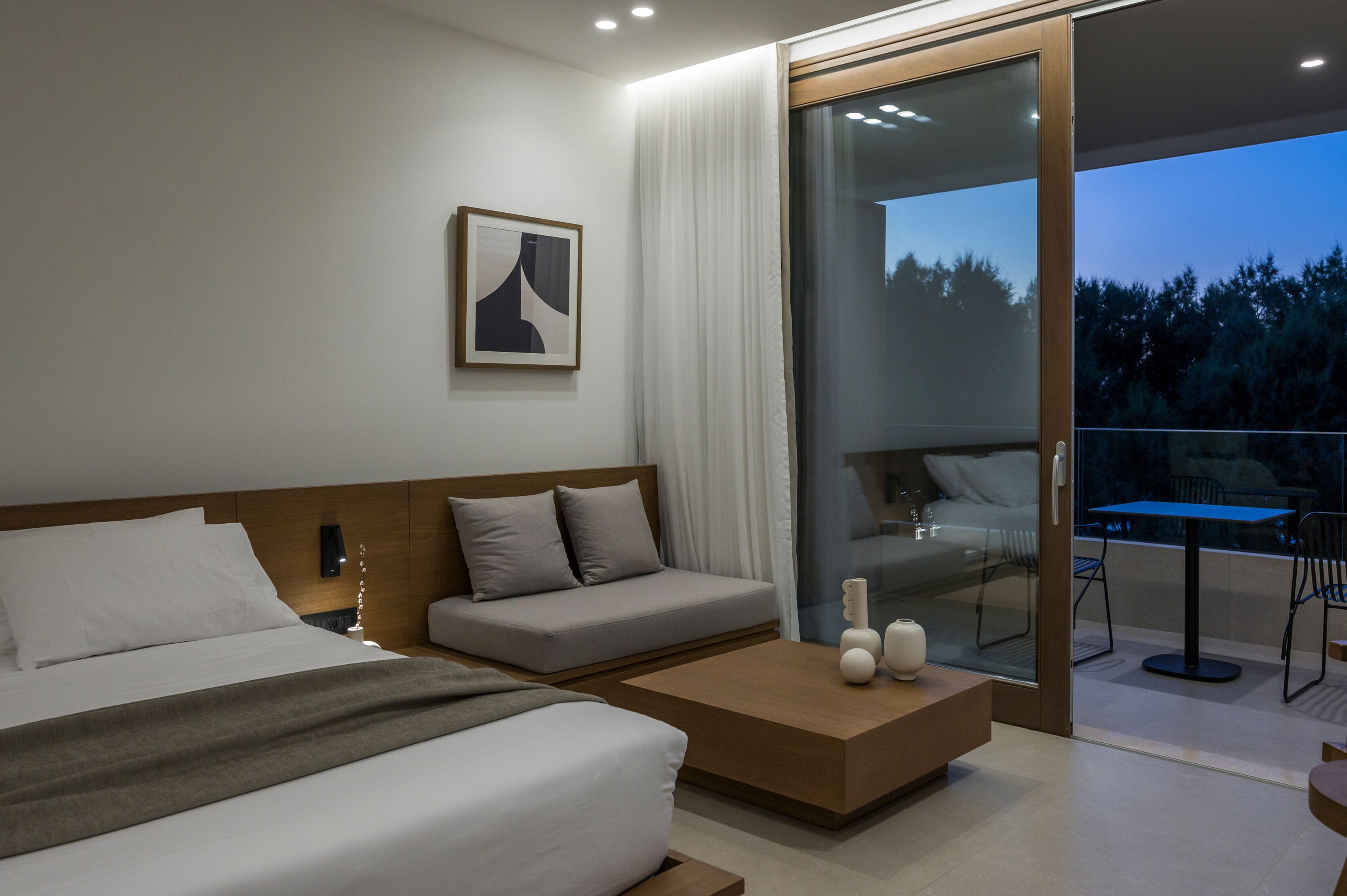 Ett modernt hotellrum med en stor säng, en soffa, ett litet bord och en balkong med bord och stolar.