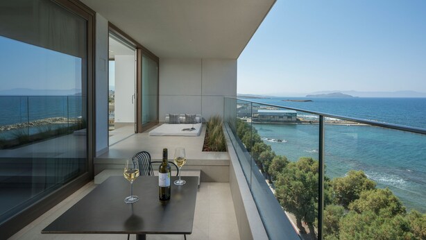 Ein Balkon mit Tisch, Weinglas und Flasche, mit Blick auf die Küste und einen klaren Himmel.