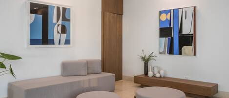 A modern room with a grey sofa, two round ottomans, a wooden bench, and abstract art on the walls.