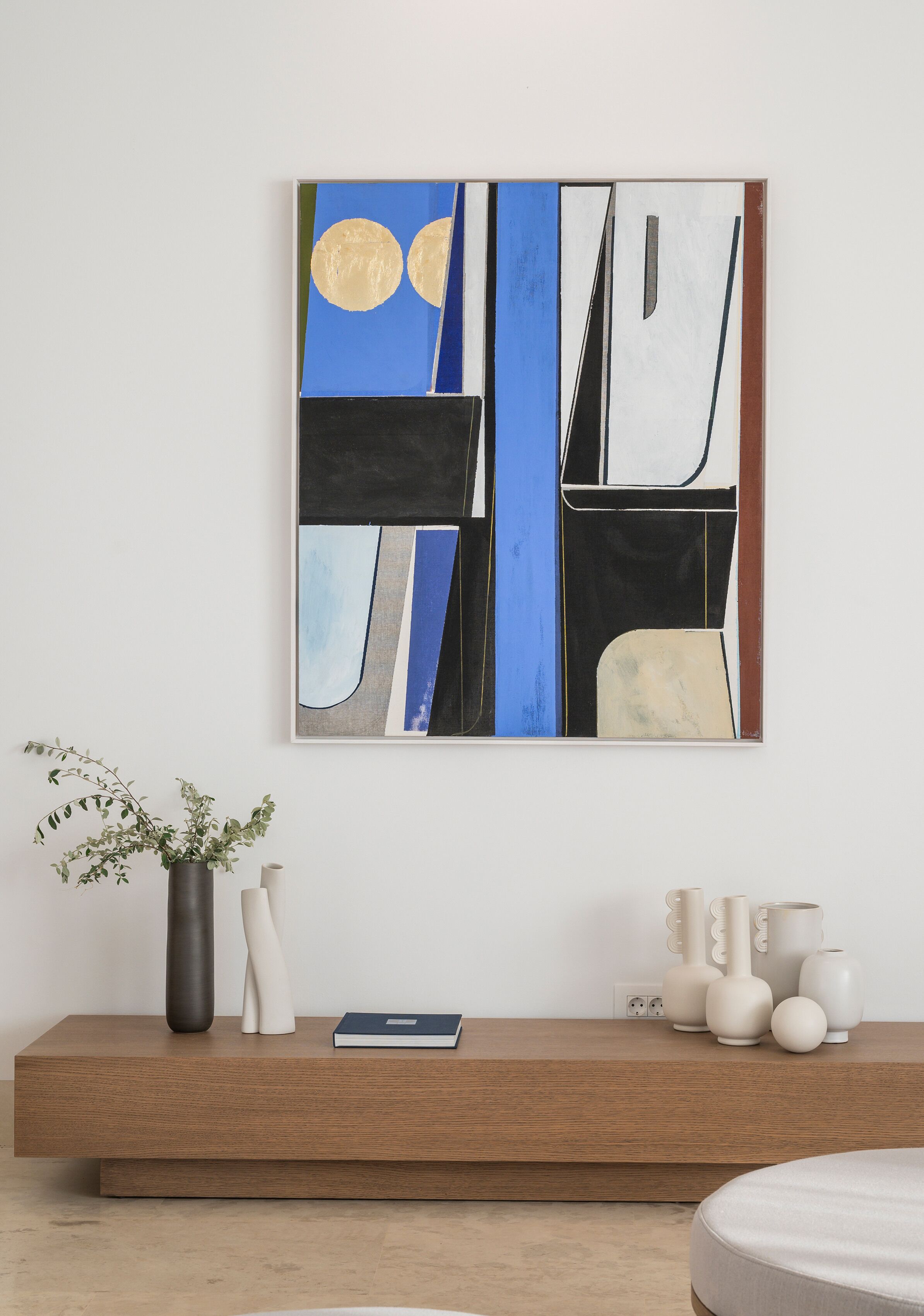 Una sala de estar moderna con un cuadro abstracto contemporáneo en la pared, una consola de madera con adornos y una planta en maceta.