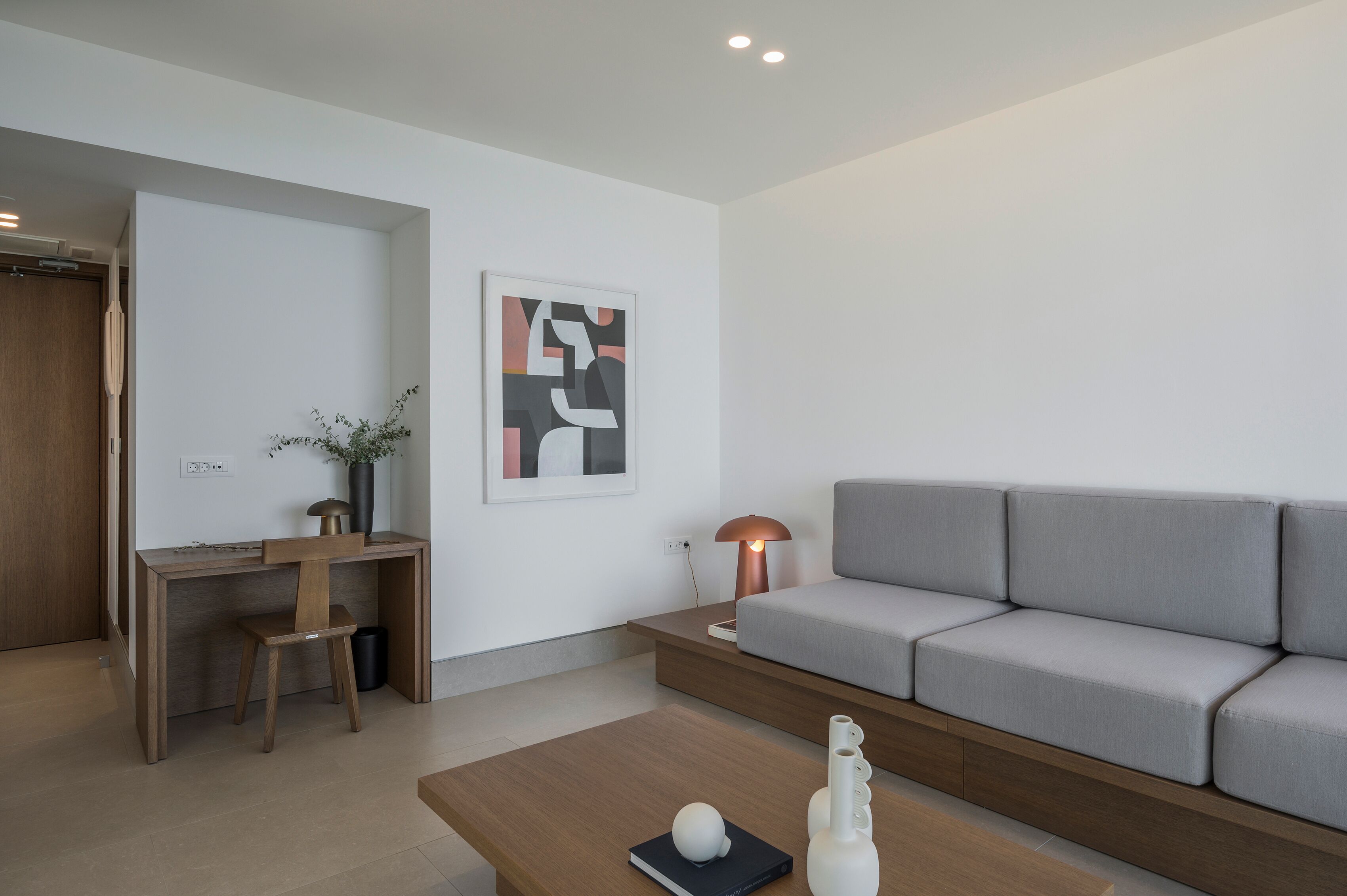A modern living room with a grey sofa, wooden desk, and a lamp.