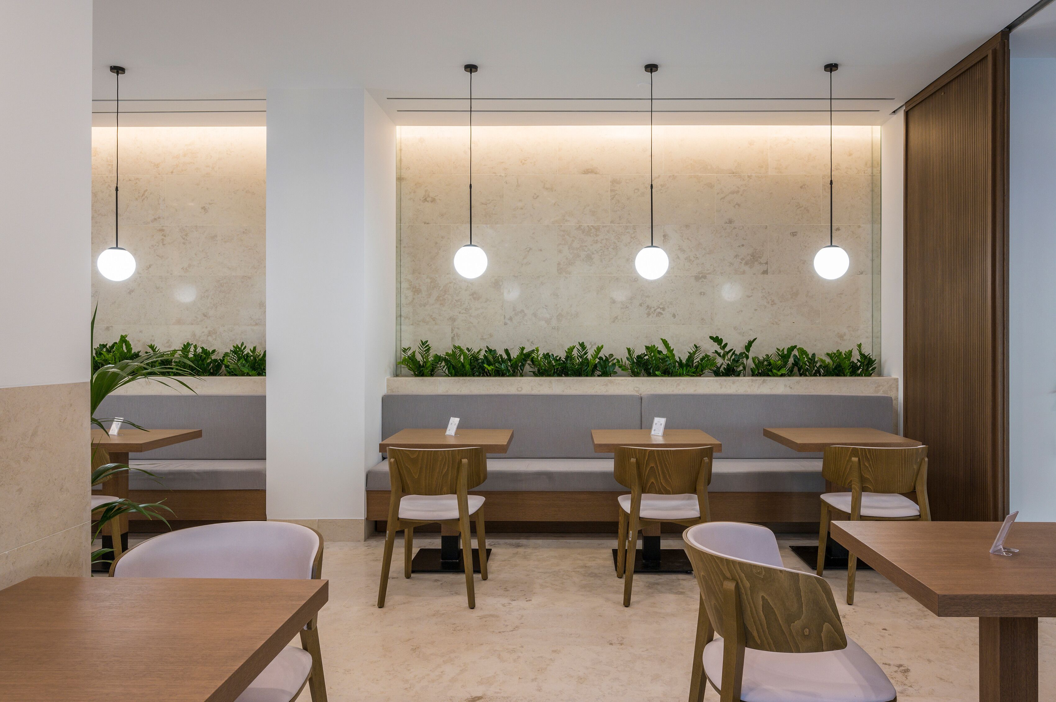 Un café moderno con mesas y sillas de madera, una zona de estar con bancos bajos y lámparas colgantes.