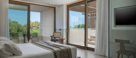 A modern bedroom with a large bed, a TV, and a balcony with a view of greenery.