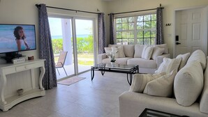 A living room with a television, a sofa, a coffee table, and a view of the outdoors.