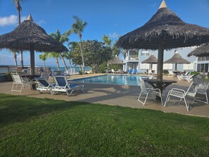 Un espace aménagé au bord de la piscine, avec des chaises longues, des parasols en chaume et une vue sur l’océan.