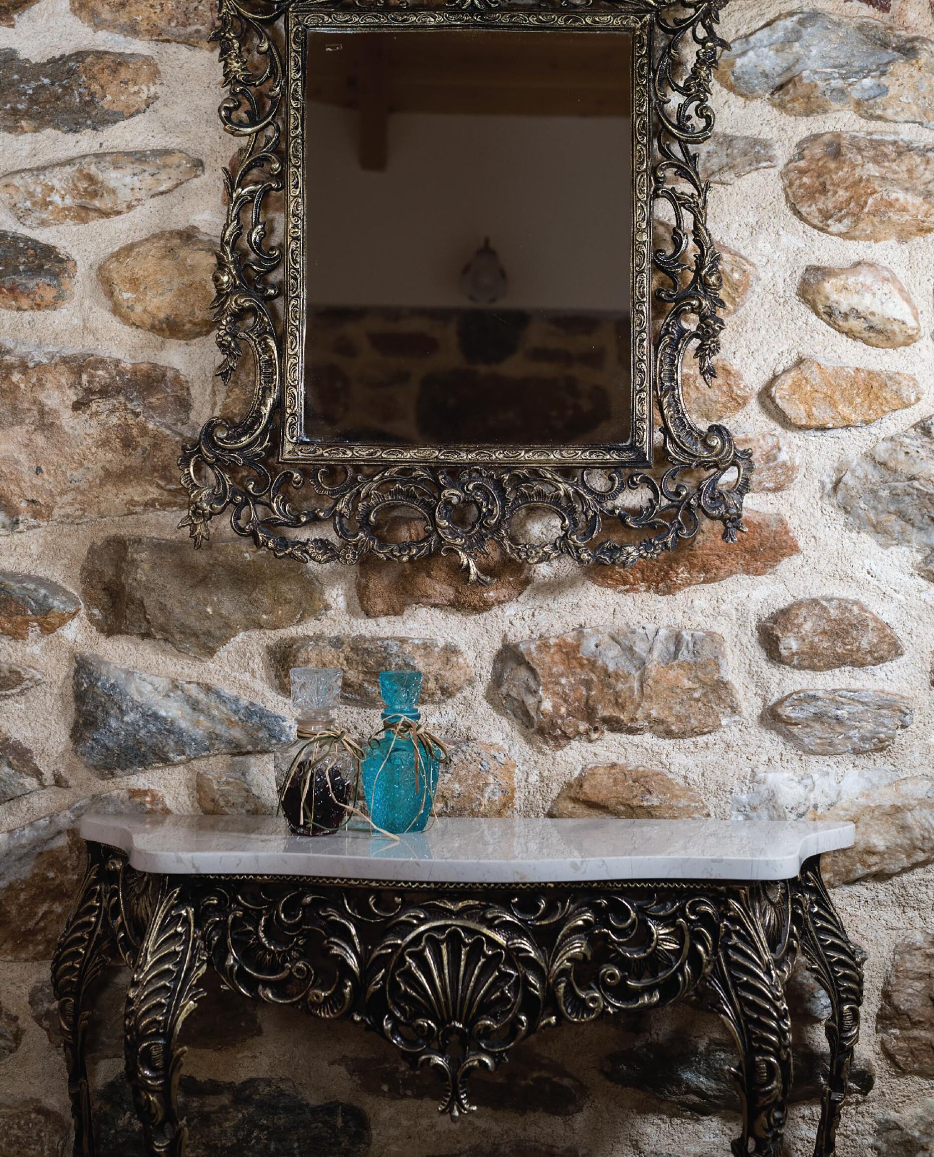 A stone wall with a decorative mirror and a marble console table with a blue bottle.