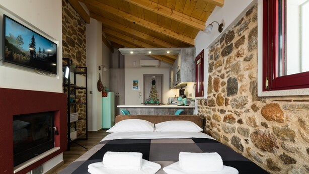 Un dormitorio con pared de piedra, chimenea, cama con ropa de cama blanca y televisión en la pared.