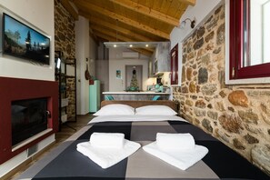 Ein Schlafzimmer mit Steinwand, Kamin, einem Bett mit weißer Bettwäsche und einem an der Wand montierten Fernseher.