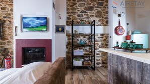 Una habitación acogedora con pared de piedra, chimenea, televisor, estante de madera y una zona de cocina con hervidor.