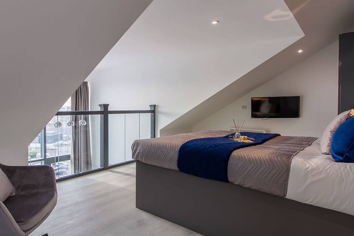 A modern bedroom with a bed, a chair, and a TV.
