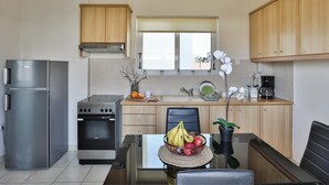 A compact kitchen with a refrigerator, stove, oven, and a dining area with a table and chairs. - Nautilus Apartments Airport by Airstay (Spata-Artemida)