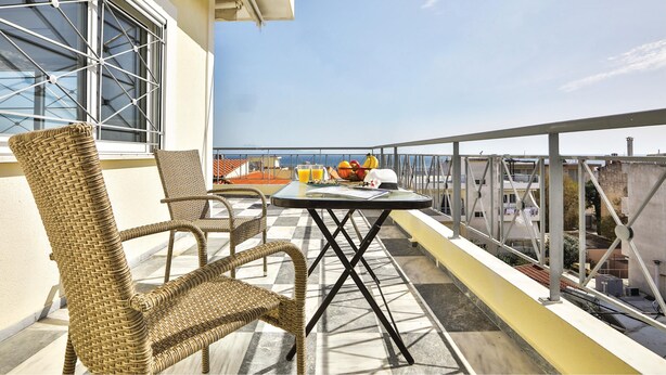 A balcony with wicker chairs, a table with fruits and drinks, and a view of the sea. - Nautilus Apartments Airport by Airstay (Spata-Artemida)