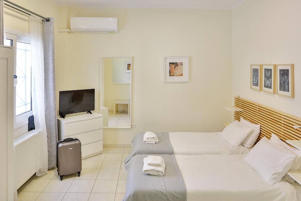 A hotel room with two beds, a TV, a dresser, a suitcase, and a window with curtains.