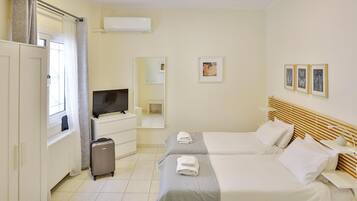 Habitación de hotel con dos camas, televisión, cómoda, maleta y ventana con cortinas.